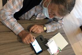 Senior sitzt am Tisch und bedient mit einem Stift sein Smartphone