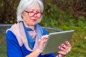 Seniorin sitzt auf der Bank und hält Tablet in der Hand