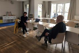 Zwei Personen sitzen an einem langen Tisch und sprechen miteinander