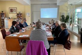 Senioren sitzen an den Tischen und schauen auf Leinwand