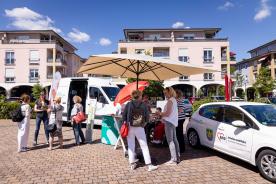 Referentin Petra Rollfing im Gespräch mit drei Damen. Daneben unterhält sich Kerstin Wasmuth mit einer Frau. Im Hintergrund steht das Engel-Mobil sowie das Auto der Arbeiterwohlfahrt. 