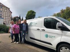 Petra steht mit zwei Seniorinnen und der Ansprechpartnerin der Caritas vor dem Info-Mobil. Sie posieren gemeinsam in die Kamera.