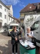 Die Besucherin und Theresa stehen auf dem Marktplatz und lächeln in die Kamera.