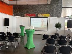 Die Titelfolie der Präsentation sowie einige Stühle und zwei Stehtische sind in der Oberrheinhalle in Offenburg zu sehen.