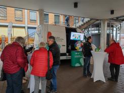 Besucher:innen stehen an Stehtischen vor dem Infomobil und unterhalten sich 