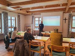 Die Teilnehmenden sitzen im Raum und blicken zur Präsentation an der Leinwand und zu unserem Referenten Johannes der neben der Leinwand steht