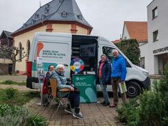 Zwei Damen sitzen vor dem Infomobil und Frau Fink steht mit einem Herrn neben dem Infomobil