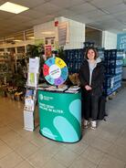 Theresa steht am Infomobilstand im Combi Supermarkt. Links hinter ihr sind Blumen, direkt hinter ihr Wassergetränkekisten.