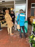 Theresa liest am Infostand zwei Besucherinnen eine Frage aus dem Digitalführerschein vor. Sie stehen zusammen vor dem Supermarkt.