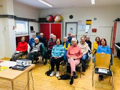 Rund 15 Senior:innen sitzen auf Stühlen in einem Raum des Kulturhofs und gucken nach vorne in die Kamera.