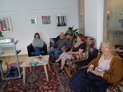 Zwei Teilnehmerinnen, ein Teilnehmer und Theresa sitzen im Ruheraum der Bibliothek auf Sesseln und lächeln in die Kamera.