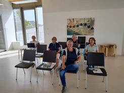 Kooperationspartner Frauke Düßmann und vier Seniorinnen sitzen auf Stühlen und gucken in die Kamera.