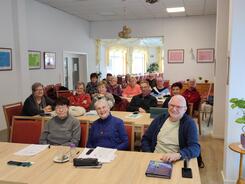 Im Plauderstübchen sitzen in vier Reihen über 15 Senior:innen und blicken nach vorne. Einige lächeln.