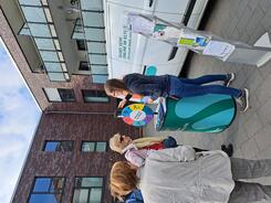 Petra steht mit dem Info-Stand vor dem Info-Mobil am Glücksrad. Drei Seniorinnen stehen um sie herum und eine Seniorin beantwortet eine Frage.