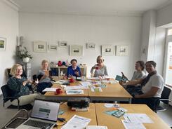 Die Teilnehmerinnen sitzen an einem Gruppentisch und halten ihr Smartphone oder eine Kaffeetasse hoch.
