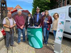 Ein Gruppenfoto mit sechs Personen an dem Info-Stand neben dem Info-Mobil (drei Senior:innen stehen links, daneben von links nach rechts: Herr Beckmann, Petra und Frau Eilert).