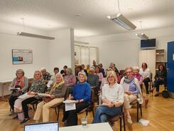 Mehrere Personen sitzen neben und hintereinander auf Stühlen im Raum und blicken nach vorne.