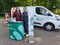 Petra (links) steht mit Frau Surhoff (rechts) am Info-Stand vor dem Info-Mobil. Die beiden posieren in die Kamera.