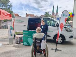 Ein Mann im Rollstuhl steht vor dem Infomobil und blickt zu Katharina.