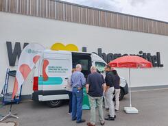 Mehrere Personen stehen vor dem Infomobil, dass vor einem Edeka-Markt platziert wurde.