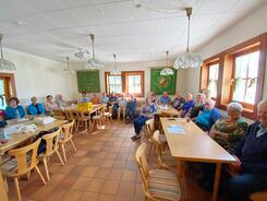 Im Schützenheim in Schmidmühlen sitzen an den Wänden auf Sitzbänken insgesamt 22 Senior:innen und blicken in die Kamera. Das Bild ist im Weitwinkelmodus, damit alle Teilnehmende rauspassen,