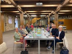 In einem Tagungsraum innerhalb der Burg Dagestein sitzen 16 Personen an einem langen Tisch. Sie blicken in die Kamera. Auf dem langen Tischen liegen Zettel und Broschüren.