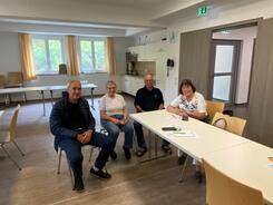 An einem Tischende sitzen zwei Männer und zwei Frauen, die lächelnd in die Kamera nach vorne blicken.
