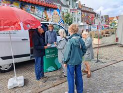 Mehrere Personen stehen vor dem Infomobil und unterhalten sich mit Referent Johannes, der hinter dem Infostand steht.