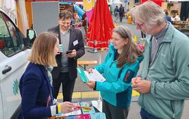 Eine Frau und ein Mann stehen am Infostand; die Frau hält einen Flyer in der Hand. 
