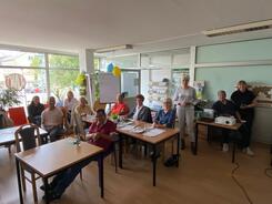 Im Treffpunkt "Nebenan" sitzen an verschiedenen Tischen elf Personen und posieren in die Kamera.