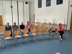 In einem großen Veranstaltungssaal im Rathaus Wiedemar sitzen sechs Personen auf zwei Stuhlreihen und blicken nach vorne in die Kamera.