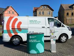 Das Info-Mobil des Digitalen Engel steht mit dem Info-Stand auf einem Parkplatz in Sandersdorf. Im Hintergrund stehen Häuser.