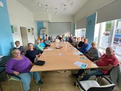 Über zwanzig Senior:innen sitzen an einem großen langen Tisch in einem Veranstaltungsraum des Nachbarschaftstreff West.