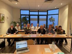 Die Teilnehmenden sitzen in zwei Tischreihen und lächeln in die Kamera.