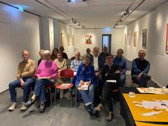 In einem Raum im Buxtehude Museum sitzen in vier Stuhlreihen 17 Personen.