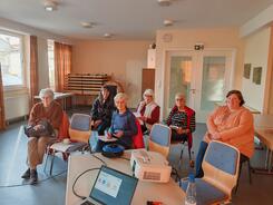 Mehrere Damen sitzen auf St&uuml;hlen verteilt in einem hellen Raum und blicken nach Vorne.
