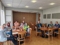 Mehrere Personen sitzen an zwei Tischen zusammen und blicken nach Vorne.