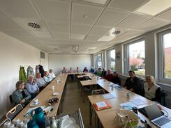 In einem Seminarraum der KVHS sitzen in U-Form Senioren ab 50 Jahren an Tischen und blicken nach vorne in die Kamera. Auf den Tischen liegen Materialien. Das Bild ist im Weitwinkelmodus aufgenommen.