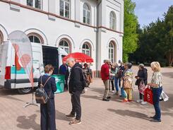 Mehrere Personen stehen auf einem Platz vor dem Infomobil und unterhalten sich.