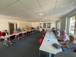 Im Weitwinkelmodus sind 16 Personen an Tischen in U-Form abgebildet. Die Menschen sind nur schwer zu erkennen, da sie klein auf dem Bild sind.