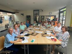 An sechs zusammengestellten Tischen sitzen auf zwei Seiten ungef&auml;hr 13 Personen. Sie blicken nach vorne in die Kamera. Auf den Tischen liegen Unterlagen.