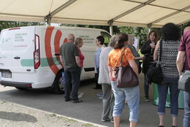 Die Besucher:innen und Theresa stehen an einem Infostand rechts neben dem Infomobil. Sie stehen unter einem Zelt.