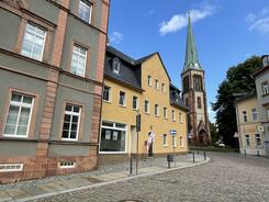 Zu sehen sind &auml;ltere Geb&auml;ude, ein bew&ouml;lkter Himmel und eine Kirche.