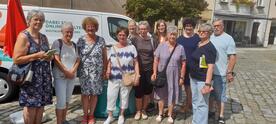 Gruppenbild von Petra (Mitte) mit acht Seniorinnen und einem Senior (rechts) sowie Ansprechpartnerin Selina Pietsch vor dem Info-Mobil