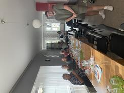 Auf dem Bild sitzen die Teilnehmenden auf der linken Seite einer langen Tischreihe, der Mitarbeiter der Lausitzer Rundschau steht recht neben der Tischreihe, Theresa sitzt am Ende der Tischreihe. Alle Personen schauen in die Kamera.