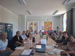 Die Teilnehmenden sitzen an einem langen Tisch und blicken in die Kamera.