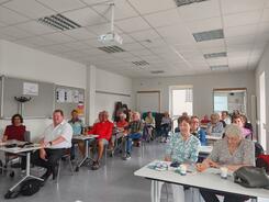 Mehrere Personen sitzen an Tischen im Raum und blicken nach vorne.