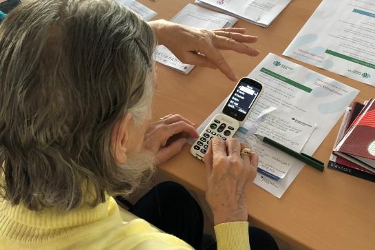 Eine Seniorin sitzt an einem Tisch und hat ein Doro Smartphone in der Hand