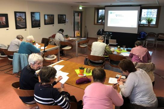 Eine Seniorengruppe sitzt am Tisch und hört einem Vortrag zu