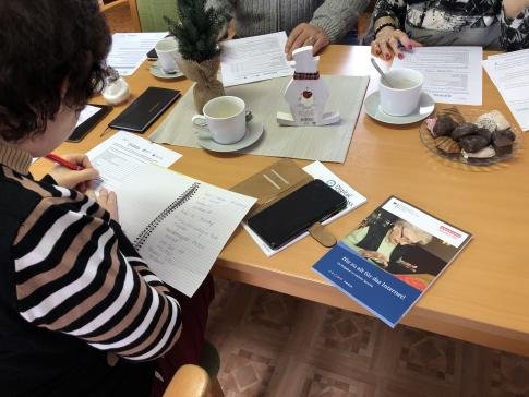 Frau am Tisch mit Smartphone und Broschüre "Nie zu alt fürs Internet"